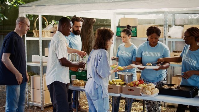 Multicultural volunteers provide free, freshly prepared meals to poor and homeless people. Individuals from non-profit organization, outdoors serving food to the needy and less privileged.