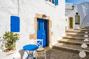 Typical white Greek house with blue door and small table with chair on narrow street in Plaka village, Milos island, Cyclades, Greece - 664105094