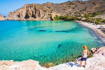 Young woman tourist standing on rock and looking at amazing Plathiena beach, Milos island,...