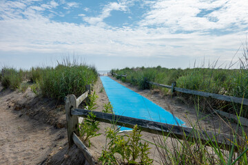 Blue traction handicapped carpet on a sandy path going over a dune towards the beach and ocean
