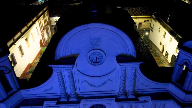 Cinematic aerial dolly shot over the facade of an antique cathedral in Santa Rosa de Copan, Honduras, and that is illuminated with blue light