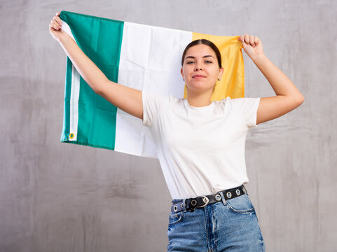 Calm cheerleader girl holds Ireland flag in her hands. Isolated on gray background