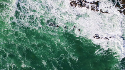 Top foaming stormy waves splashing on coastal stones. Drone beautiful ocean