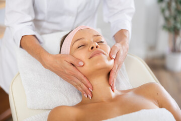 Portrait of young female client getting soothing and relaxing facial massage to help relieve...