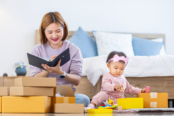 Young Asian mother is packing her merchandise product package while working at home ready to deliver while her toddler kid is playing around with her toy