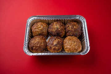 Juicy Fresh Beef Meat Patties in Disposable Foil Packaging on a Red Background.