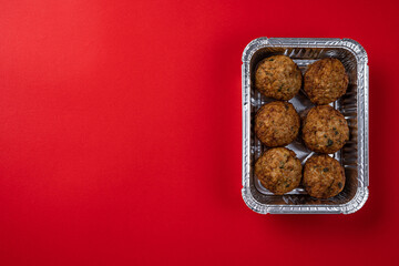 Juicy Fresh Beef Meat Patties in Disposable Foil Packaging on a Red Background.