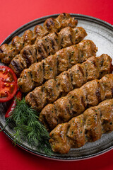 Lule Kebab Meat Dish on a Gray Plate with Tomatoes on a Red Background.