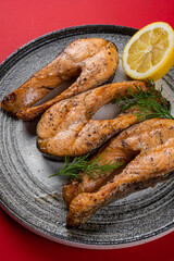 Grilled Fish Steaks on a Gray Round Plate on a Red Background.
