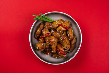 Chicken Drumsticks and Wings in Spicy Teriyaki Sauce with Sesame Seeds on a Gray Plate on a Red Background