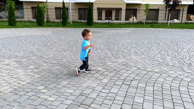 Healthy active baby boy runs by the paved street. Cute kid in t-shirt and pants is on the walk in summer.