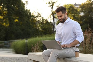 Handsome young man using laptop on stone bench outdoors. Space for text - obrazy, fototapety, plakaty