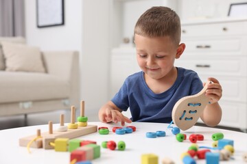 Motor skills development. Little boy playing with wooden lacing toy at white table indoors