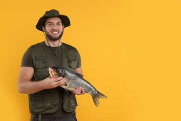 Fisherman with caught fish on yellow background, space for text