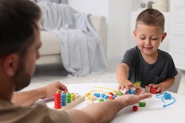 Fototapeta premium Motor skills development. Father and his son playing with wooden pieces at table indoors