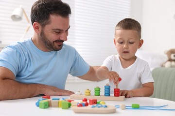 Motor skills development. Father and his son playing with stacking and counting game at table indoors