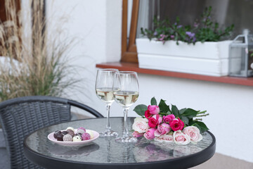 Bouquet of roses, glasses with wine and candies on glass table on outdoor terrace
