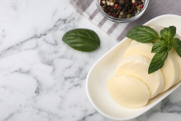 Plate with tasty mozzarella slices and basil leaves on white marble table, above view. Space for text