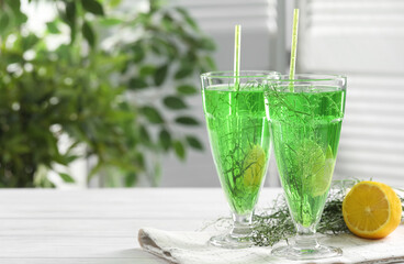 Glasses of homemade refreshing tarragon drink, sprigs and lemon on white wooden table, space for text