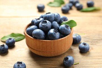 Bowl of tasty fresh blueberries on wooden table, closeup