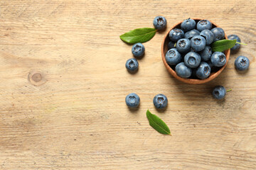 Bowl of tasty fresh blueberries with leaves on wooden table, flat lay. Space for text