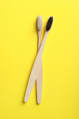 Two bamboo toothbrushes on yellow background, flat lay