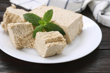 Plate with pieces of tasty halva and mint on wooden table, closeup