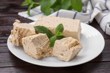 Plate with pieces of tasty halva and mint on wooden table, closeup