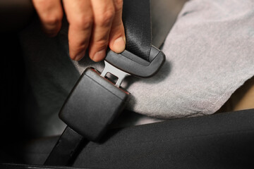 Man fastening safety seat belt in car, closeup