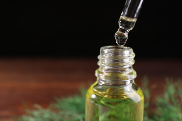 Dripping dill essential oil from pipette into bottle on table, closeup. Space for text