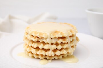 Tasty waffles with condensed milk on plate, closeup