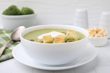 Delicious broccoli cream soup with croutons, sour cream and pumpkin seeds served on white tiled table, closeup