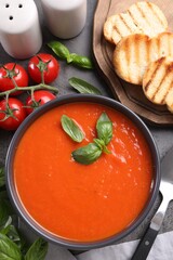 Flat lay composition with delicious tomato cream soup in bowl on grey table