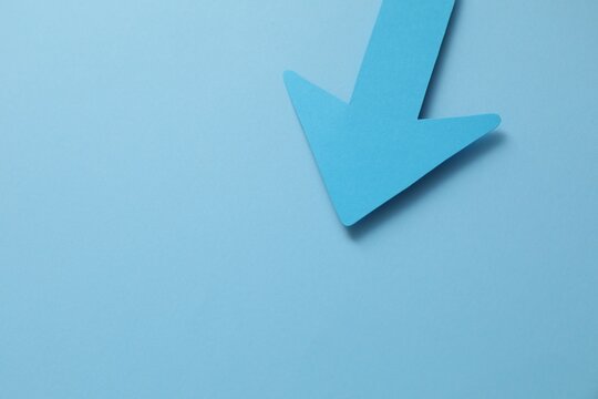 One paper arrow on light blue background, above view. Space for text