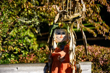 Smiling girl scarecrow with braids leaning against a wood fence, cheerful fall celebration for Halloween and Thanksgiving

