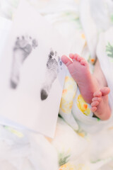 A closeup of a newborn's two feet with the toes and bottom of feet next to his/her newborn footprint from the hospital.