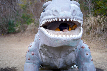 遊具の恐竜の口から外を覗く男の子 / Boy looking out of the dinosaur's mouth on the...