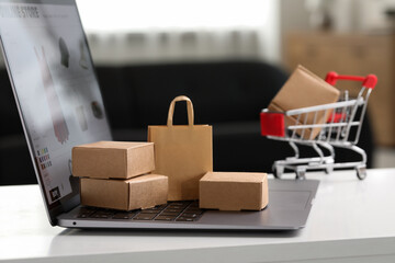Online store. Laptop, small parcels and shopping bag on white table