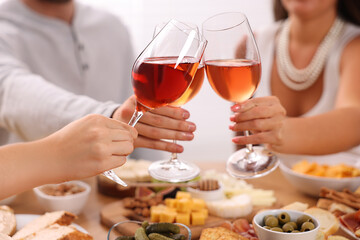 People clinking glasses with rose wine above wooden table indoors, closeup