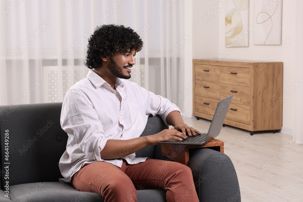 Canvas Prints Happy man using laptop on sofa with wooden armrest table at home