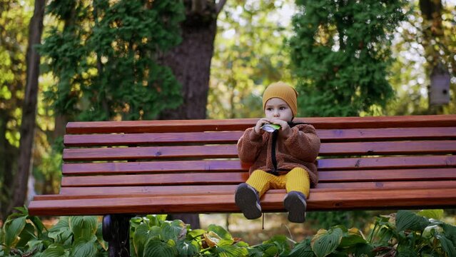 Beautiful Caucasian kid eating fruit puree from doypack. Healthy snack during walk in the park.