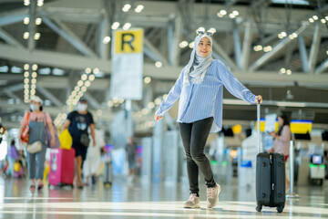 An Asian Muslim wearing a blue hijab is preparing for a vacation and she is at the international airport. She is waiting for her friends, Muslim travelers, holiday concept.
