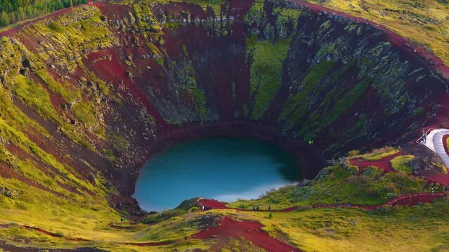 Kerid crater in Iceland, water at the bottom, red earth, vegetation and a fir forest in the background