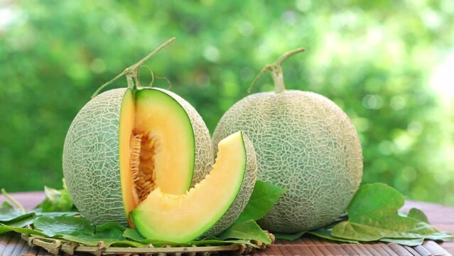 Orange Melon on blurred greenery background, Orange Melon or Cantaloupe fruit in Bamboo mat on wooden table in garden.