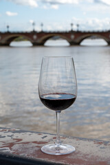 Tasting of Bordeaux blended red wine with wine city Bordeaux on background, left bank of Gironde Estuary, France. Glass of red French wine.
