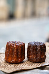 Canele, French pastry flavored with rum and vanilla, soft and tender custard center and  dark, caramelized crust specialty of Bordeaux region, France, streets of Bordeaux on background