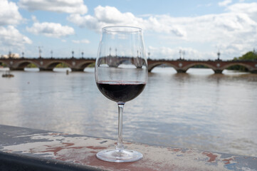 Tasting of Bordeaux blended red wine with wine city Bordeaux on background, left bank of Gironde Estuary, France. Glass of red French wine.