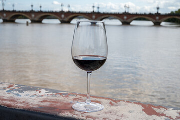 Tasting of Bordeaux blended red wine with wine city Bordeaux on background, left bank of Gironde Estuary, France. Glass of red French wine.