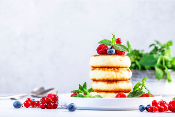 Thick pancakes with cottage cheese and blueberries, raspberries, red currants with fresh mint leaves on white plate. Gray table background