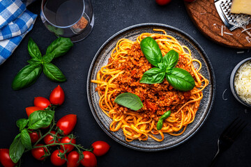 Spaghetti bolognese or pasta with minced meat and tomato sauce with green basil leaves on black table background, top view
